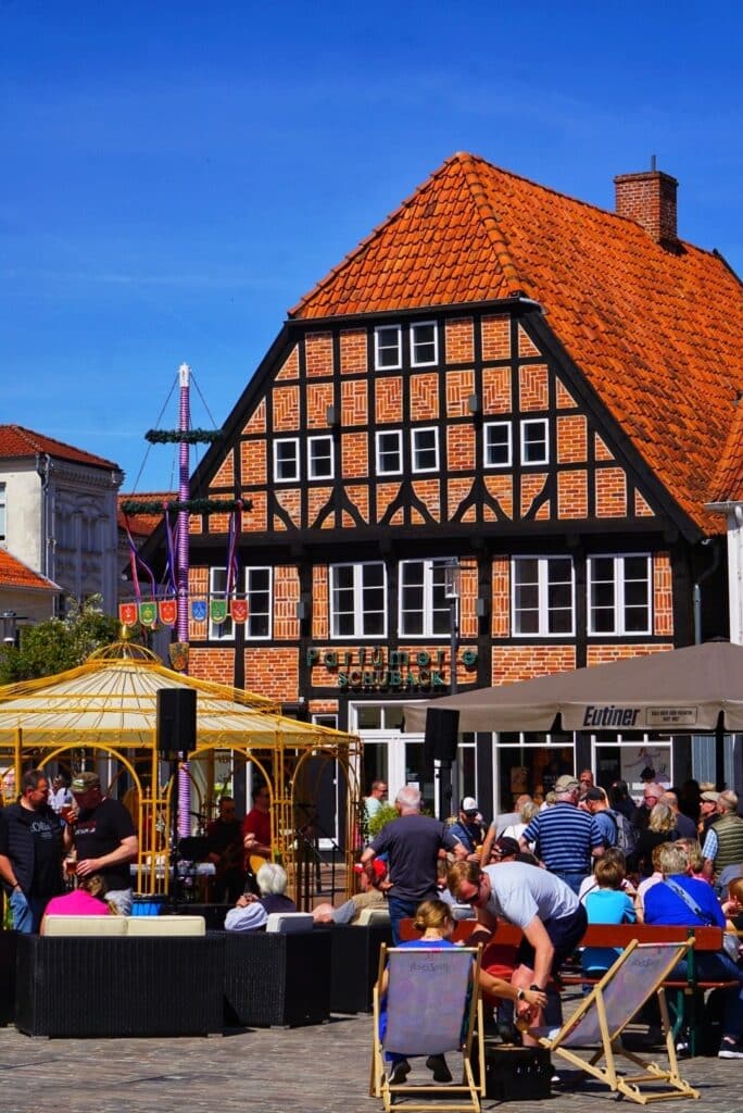 **Alt-Text für RankMath SEO:** Belebter Marktplatz in Eutin mit historischem Fachwerkhaus, Brauerei und Festbetrieb an einem sonnigen 01. Mai.